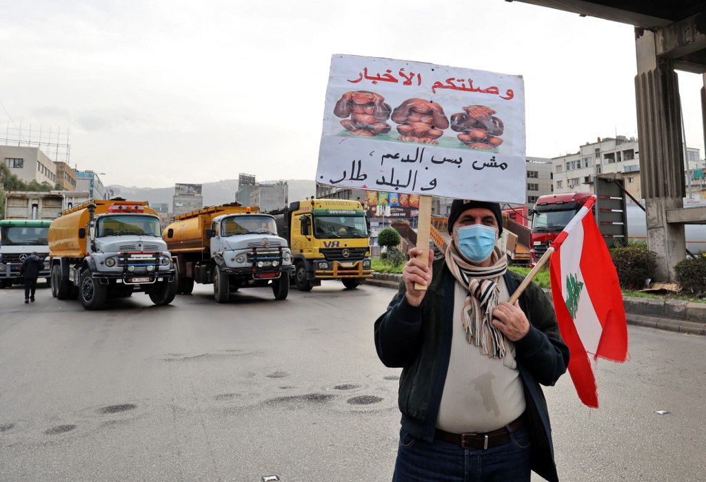 Un manifestant libanais tient une pancarte alors que des camions bloquent une route à Beyrouth, la capitale du Liban, le 13 janvier 2022. (Photo, AFP)