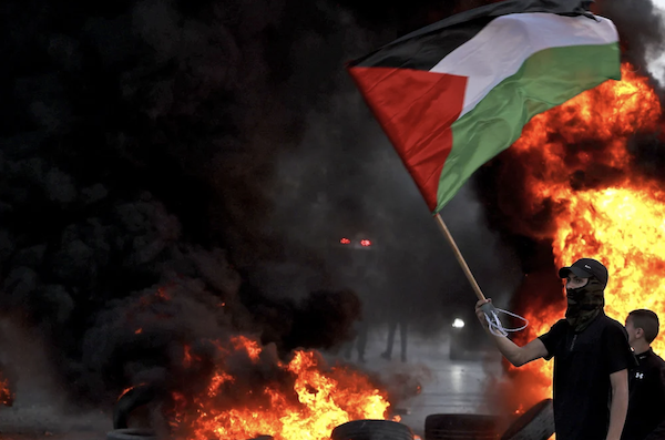 仮面をかぶった抗議者が、イスラエル軍との衝突中に燃えるタイヤの近くでパレスチナの旗を振っており、年に一度の民族主義者の旗がエルサレムを通過する行進を非難した後.  (AFP)