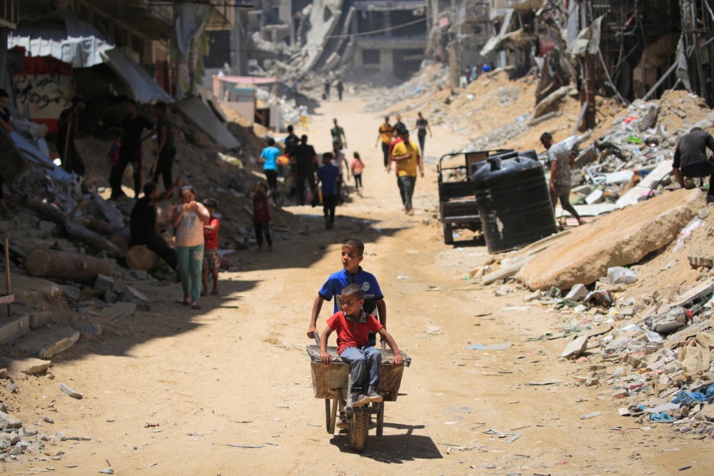 Un enfant palestinien pousse un autre enfant dans une brouette entre des bâtiments détruits à Khan Yunis, dans le sud de la bande de Gaza. (AFP)