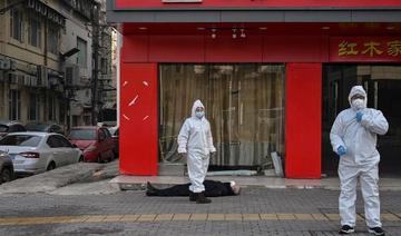 Cette photo prise le 30 janvier 2020 montre des fonctionnaires en tenue de protection vérifiant un homme âgé portant un masque facial qui s'est effondré et est décédé dans une rue près d'un hôpital de Wuhan. (Hector Retamal/AFP)