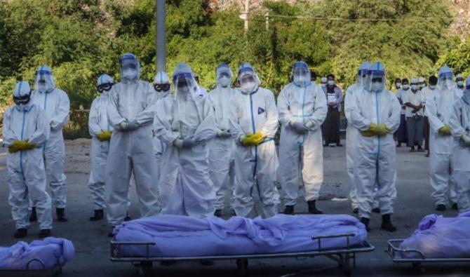 Des volontaires portant des équipements de protection individuelle (EPI) prient devant les corps de personnes décédées du coronavirus Covid-19 lors de leurs funérailles dans un cimetière de Mandalay le 14 juillet 2021.(STR / AFP)