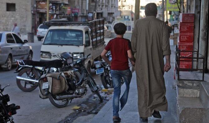 Un syrien déplacé, Mustafa Shaaban Abu Khalil, marche aux côtés de son fils qui a perdu une jambe à cause d'un bombardement, dans une rue de la ville rebelle d'al-Bab, au nord-ouest d'Alep, dans le nord de la Syrie, le 23 juin 2021. (AFP)