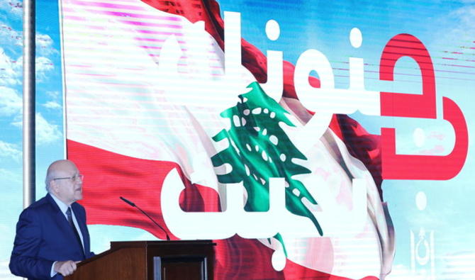 Le Premier ministre libanais, Najib Mikati, prenant la parole près du slogan «Nous t’aimons dans ta folie» affiché sur un écran au Grand sérail de Beyrouth, jeudi. (Reuters) 