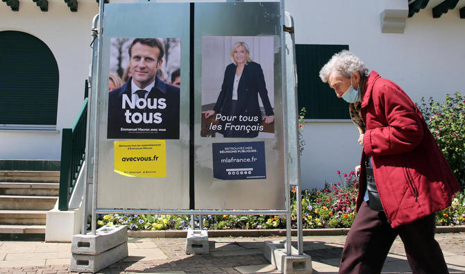 Une femme passe devant les affiches de la campagne présidentielle du président et candidat centriste Emmanuel Macron ainsi que la candidate d'extrême droite Marine Le Pen, à Anglet, le 16 avril 2022. (Photo, AP) 