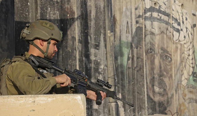 Un soldat israélien monte la garde alors que des Palestiniens attendent au poste-frontière de Qalandia, entre la Cisjordanie occupée et Jérusalem. (AFP)