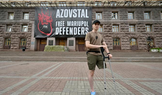 S'appuyant sur des béquilles après l'amputation de sa jambe gauche, Vladyslav, 29 ans, parle devant une immense affiche accrochée à la façade de la mairie de Kiev sur laquelle on peut lire «Libérez les défenseurs de Marioupol». (Photo, AFP)