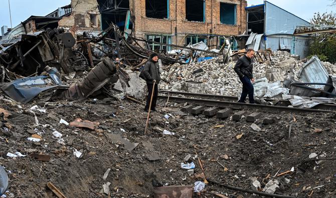 Les gens se tiennent près d'un cratère à côté d'une gare de fret à Kharkiv, qui a été partiellement détruite par une frappe de missile, le 28 septembre 2022. (Photo, AFP)