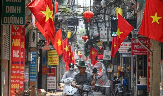 Un homme porte un ventilateur par une chaude journée alors qu'il conduit une moto dans une rue bordée de drapeaux nationaux vietnamiens à Hanoï, le 30 avril 2024. La chaleur extrême qui sévit dans certaines parties de l'Asie du Sud et du Sud-Est a incité les autorités à lancer des avertissements sanitaires alors que des températures élevées sont enregistrées dans toute la région. (Photo Nhac Nguyen AFP)